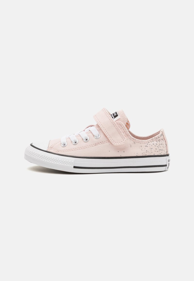 Zapatilla de lona rosa con cordones blancos y una correa de Velcro. Presenta una puntera de goma y líneas de acento negras en la suela.