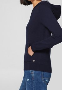 Marineblauwe hoodie van zacht stof, met een voorzak, trekkoordkap en een kleine metalen logobezet. Klassieke pasvorm.