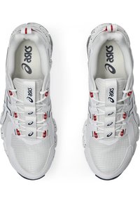 Zapatillas deportivas blancas con un diseño texturizado, que presentan detalles en rojo, elementos reflectantes y una suela acolchada. Logo visible en la lengüeta.