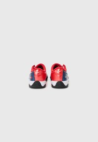 Red and navy athletic shoes featuring a smooth synthetic upper, padded collar, white midsole, and textured black rubber outsole.