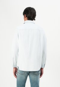 Lys blå langermet skjorte med avslappet passform, knapper på ermene og en ryggdetalj, kombinert med falmede blå jeans.