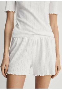 Ensemble en coton blanc composé d'un haut à manches courtes et d'un short. Le tissu présente un motif texturé avec des bords festonnés et des rayures verticales.