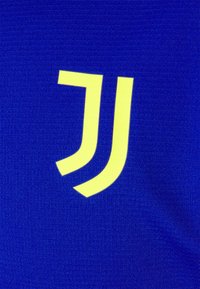 Blauer Stoff mit einem gelben "J"-Logo und zwei geschwungenen Akzenten, der eine glatte Textur und ein einfaches Design zeigt.