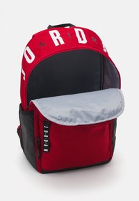 Piros és fekete hátizsák nagy fehér "JORDAN" logóval, cipzáros rekeszekkel, szürke belső béléssel és állítható vállpántokkal.