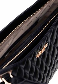 Bolso de mano negro acolchado con una textura suave, que presenta herrajes en tono dorado y múltiples compartimentos con cremallera forrados con una tela a rayas.
