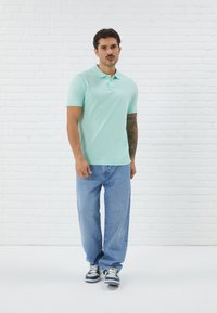 Lys mintgrønn polo-shirt med krage, brukt sammen med lyseblå straight-leg jeans og grå joggesko. Glatt stoff, avslappet passform.