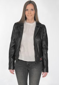 Schwarze Leder-Motorradjacke mit tailliertem Design, Reißverschlusstaschen und kontrastierenden roten und weißen Streifen am Saum. Getragen über einem hellen Oberteil.