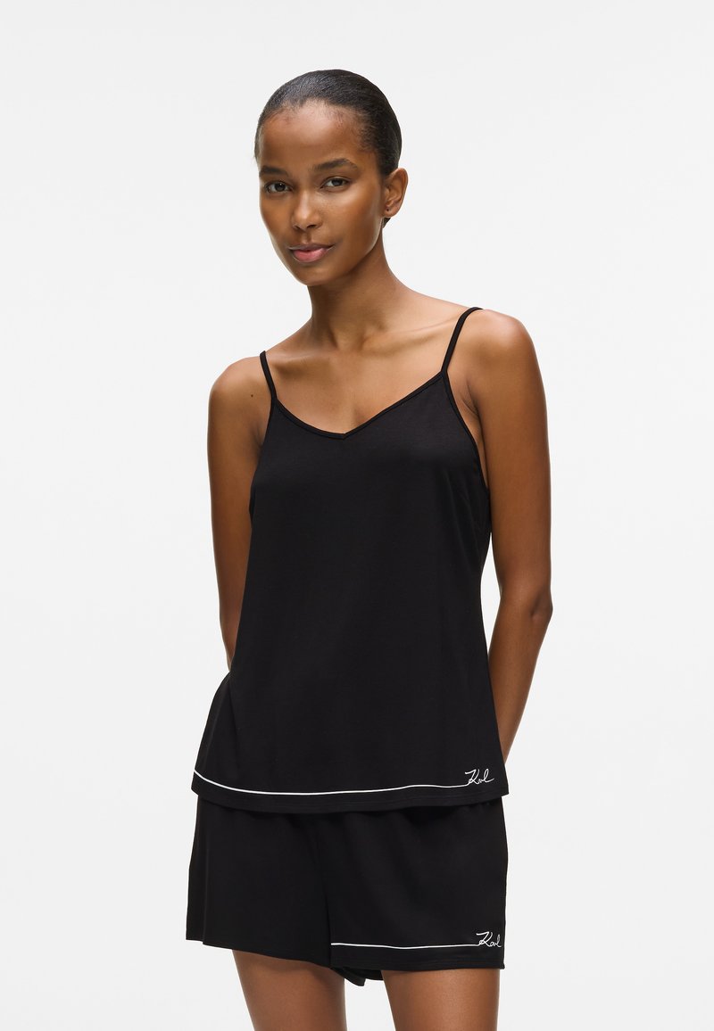 Sort ærmeløs top med V-udskæring og løs pasform, parret med matchende sorte shorts med en hvid kantdetalje i kanten.