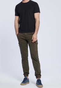 Czarna koszulka z krótkim rękawem zestawiona z oliwkowozielonymi spodniami bojówkami z bocznymi kieszeniami i elastycznymi mankietami, uzupełniona niebieskimi trampkami.