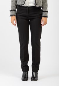Pantaloni neri con una vestibilità sartoriale, caratterizzati da sottili pieghe frontali e tasche laterali, realizzati in un tessuto morbido. Indossati con stivali alla caviglia.