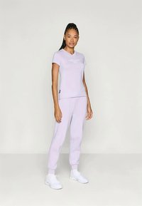 Γαλάζιο αθλητικό σετ που περιλαμβάνει μπλούζα με κοντά μανίκια και λογότυπο, καθώς και ταιριαστά παντελόνια. Ο ιστός φαίνεται λείος με άνετη εφαρμογή.