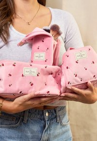 Bolsas de cosméticos de terciopelo rosa con patrones de cerezas; incluyen un diseño con cremallera y etiquetas. Las bolsas están unidas, mostrando su textura.