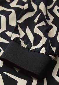 Tela estampada en negro y crema con un puño negro elástico, que presenta formas abstractas y una textura suave.