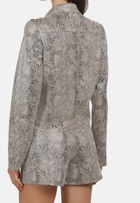 Ensemble composé d'une veste et d'un short au motif serpent, dans des nuances de gris, avec un col, des manches longues et une coupe ajustée. Fini texturé et lisse.