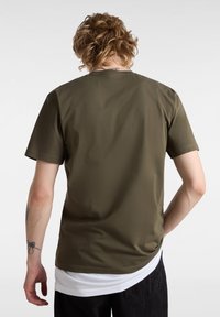 Camiseta de manga corta verde olivo con una textura suave, que presenta un cuello redondo y un look en capas sobre una camisa blanca debajo.