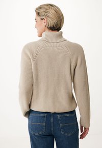 Beige turtleneck sweater with a textured knit, featuring raglan sleeves and a ribbed collar, paired with dark blue jeans with back pockets.