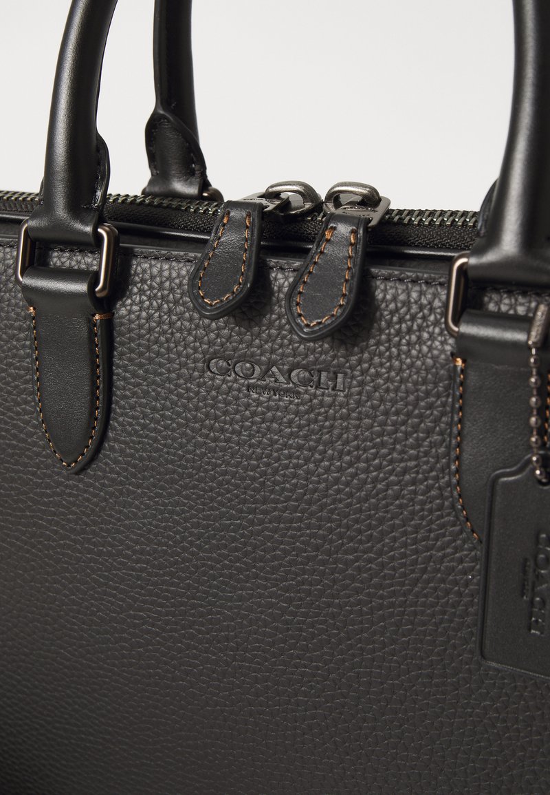 Borsa a tracolla in pelle nera con texture a grana, dotata di manici corti doppi, zip in metallo e logo del brand incastonato discretamente sul davanti.