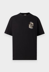 Camiseta de algodón negra con un pequeño diseño gráfico en el lado izquierdo del pecho, con el texto "GUESS" y una fecha de establecimiento en un color contrastante.