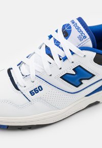 Baskets New Balance 550 blanches et bleues avec lacets blancs, côtés perforés et logo bleu près du talon et sur la languette.