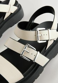 Sandali platform bianchi in pelle con due cinturini regolabili, fibbie argentate e finitura testurizzata. Suola in gomma nera, design minimalista.