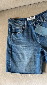 Farkkushortsit keskipitkässä sinisessä värissä, joissa on revitty helma. Edessä tasku ja vyötärölle kiinnitetty etiketti. Puuvillamateriaali, rento muotoilu.