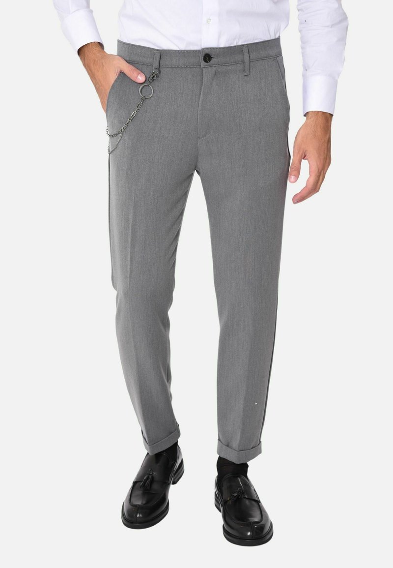 Pantaloni grigi su misura con una vestibilità slim, caratterizzati da un'accento a catena in vita, texture liscia e orli arrotolati. I mocassini neri completano il look.