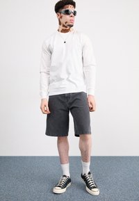 Camisa blanca de manga larga, pantalones cortos de mezclilla gris oscuro, zapatillas negras, calcetines blancos en capas y gafas de sol. Diseño simple sin patrones.