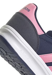 Kadar detalj s petom Adidas tenisice s ružičastim kožnim akcentima, tamnoplavom tkaninom, sivim antilopom i bijelim Cloudfoam potplatom.
