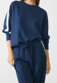 Felpa blu navy con strisce bianche ai lati, con collo rotondo e maniche lunghe, abbinata a pantaloni della tuta blu navy con vita elastica.