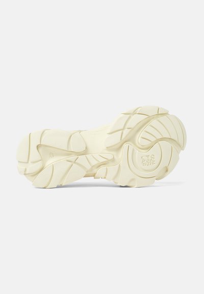 Cream-colored sneaker sole with textured rubber for traction, featuring wavy patterns and grooves for flexibility and comfort.