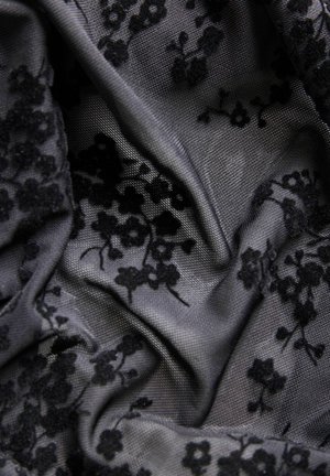 Tela de encaje floral negra drapeada, con una superficie texturizada y flores negras dimensionales sobre un fondo gris. Apariencia detallada y con capas.