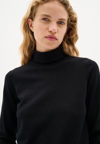 Maglione nero a dolcevita in un knit morbido e liscio; design aderente con dettagli a coste sul colletto e sui polsini. Stile minimalista.