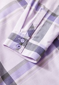 Tela de camisa de cuadros en tono púrpura claro con acentos en gris y púrpura más oscuro. Presenta un puño abotonado con dos botones a juego y una textura suave.