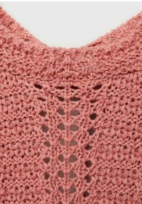 Virkmönster på plagg i en mjuk korallfärg, med öppet arbete och texturerad stickdetalj runt halslinningen.