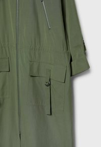 Olive green jacket featuring a front zip closure, two large patch pockets, and a cinched waistband with a decorative hardware detail.
