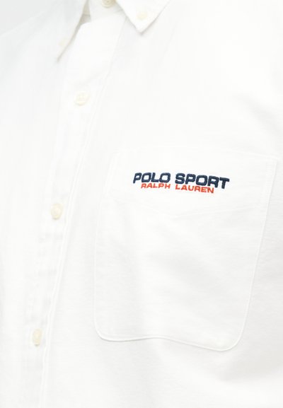 Λευκό πουκάμισο με κουμπιά και τσέπη στο στήθος κεντημένη με το κείμενο "POLO SPORT RALPH LAUREN" σε ναυτικό μπλε και κόκκινο.