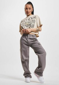 Beige cropped t-shirt with black graphic text; gray cargo pants with side pockets; white platform sneakers with pink accents.