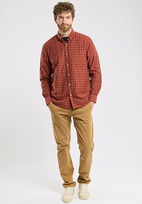 Chemise à carreaux rouges avec boutons et manches longues, associée à un pantalon beigne et des baskets crème. La chemise est en tissu doux et texturé.