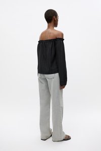 Svart avskrevet bluse med volangkant og hvite vertikale striper, sammen med lysegrå vide bukser og sandaler.
