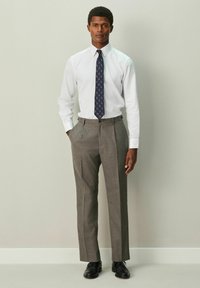 Bela srajca z dolgimi rokavi in teksturiranim zaključkom, kombinirana s sivimi hlačami z nagubanim robom. Vključuje modro kravato z geometričnim vzorcem in črne čevlje.