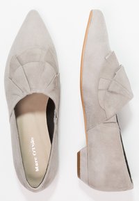 Lichtgrijze suède platte schoenen met puntige neus, decoratieve gevouwen overlays bovenop en lage bruine hakken.