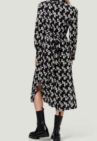 Robe chemise à motifs noir et blanc avec des manches longues, taille cintrée, fentes latérales et ourlet jusqu'aux chevilles. Portée avec des bottes épaisses noires.