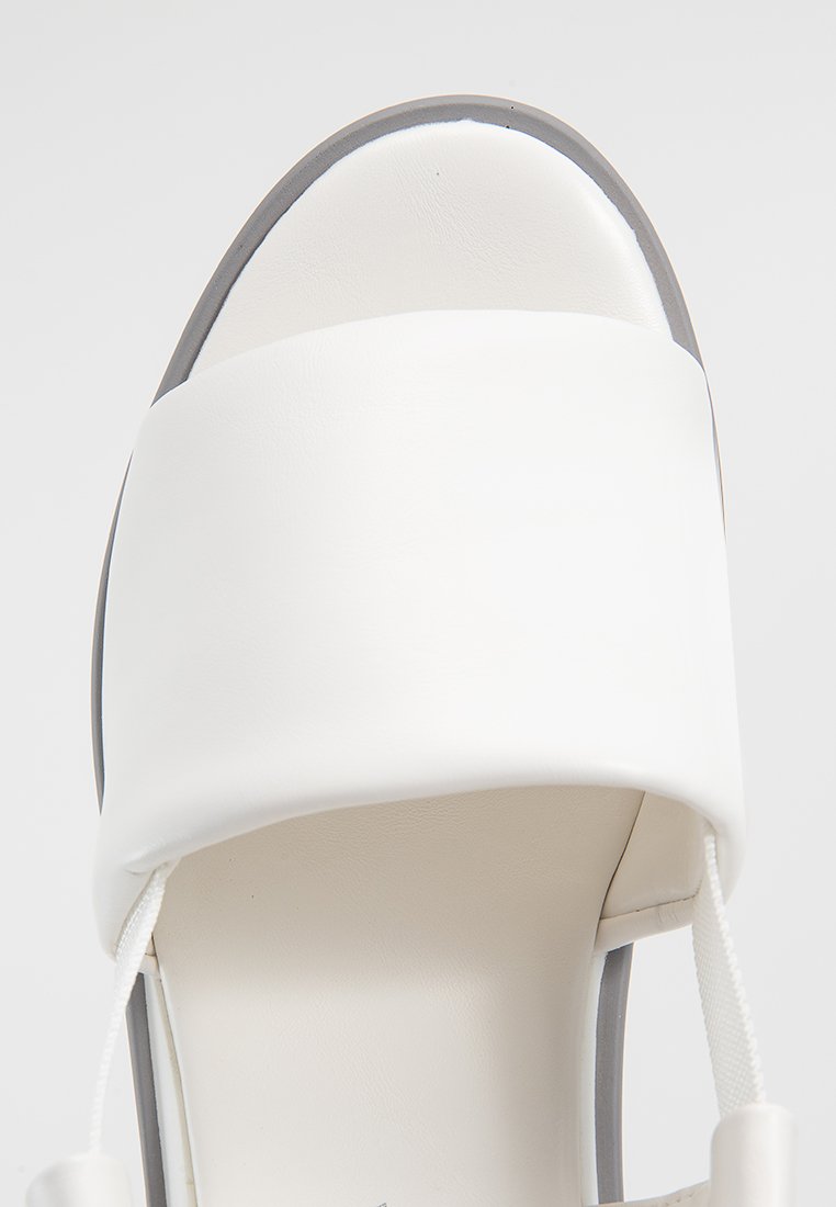 Infradito bianco con ampia fascia sulle dita, soletta imbottita e bordo grigio lungo il margine, mostrato dall'alto su uno sfondo bianco.