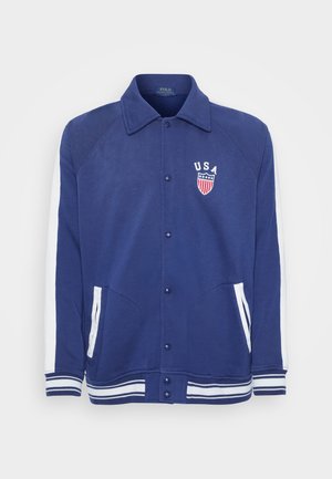 Navy blue jacket with white accents, button closure, and side pockets. Features a "USA" emblem with stars and stripes, ribbed cuffs and hem.