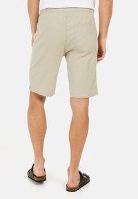 Beige shorts lavet af letvægtsstof, med elastisk talje og en enkelt baglomme. Bæres med sorte slip-on sandaler.