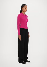 Roze langemouwen cardigan met knoopdetails, gecombineerd met zwarte wijde broek. Platte schoenen met decoratieve accenten maken de outfit compleet.