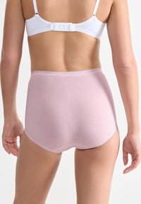 Bielizna o wysokim stanie w jasnoróżowym kolorze, wykonana z miękkiego materiału, charakteryzująca się gładką teksturą i subtelnymi, falbaniastymi krawędziami w pasie oraz na nogawkach.