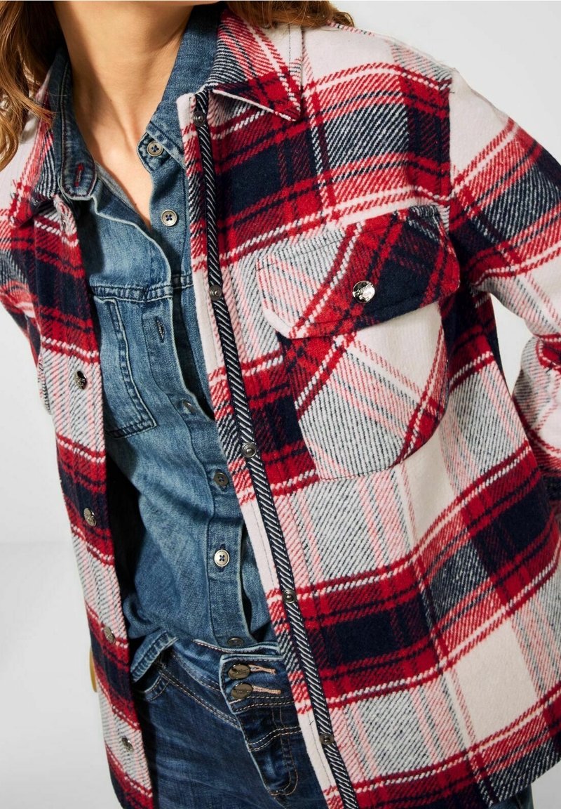 Rood, marineblauw en wit geruite flanellen shirt met een knoopsluiting aan de voorkant, met een pocket op de linkerborst en een denim shirt eronder.