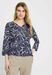 Marineblauwe blouse met een bladpatroon in lichtgrijs, voorzien van een V-hals en driekwart mouwen. Gemaakt van een zachte, gestructureerde stof.