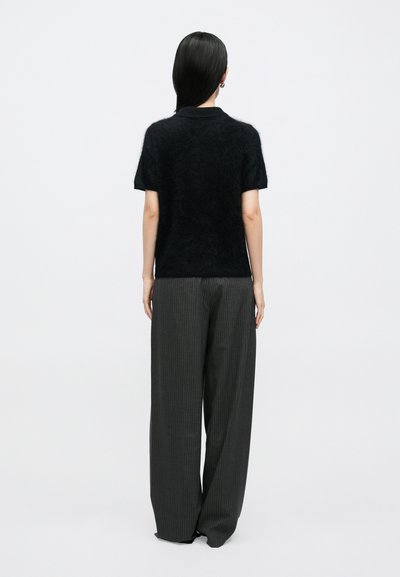 Sort, blød strikket top med korte ærmer kombineret med højttaljede, vidtbenede grå bukser med smalle striber. Enkel og minimalistisk design.